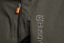 The Husqvarna Xplorer Shell Jacket, available in grape purple and aubergine purple for women, is crafted from 4-way stretch material. It features a front zipper, two zippered pockets, and a logo on the left sleeve. The chest showcases the text "BUSHMAN" vertically. With its wind and water repellent qualities, it also includes orange-accented zippers and a removable hood for versatility.