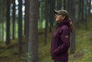 The Husqvarna Xplorer Shell Jacket, available in grape purple and aubergine purple for women, is crafted from 4-way stretch material. It features a front zipper, two zippered pockets, and a logo on the left sleeve. The chest showcases the text "BUSHMAN" vertically. With its wind and water repellent qualities, it also includes orange-accented zippers and a removable hood for versatility.