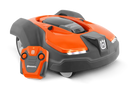 Introducing the Toy 450X Automower with RC control by Husqvarna Toys, this brightly colored orange and black robotic lawn mower showcases a sleek design complete with LED lights and compact wheels. Resembling the agility of a road bike, it comes with an orange remote control that proudly displays the Husqvarna logo on both the mower and the remote.