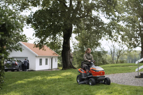 The Husqvarna Battery TS 100i Tractor, in orange with a black seat and steering wheel, offers ergonomic comfort and features robust wheels with visible blade housing. The brand logo is prominently displayed on the side, ensuring efficient mowing with every use.