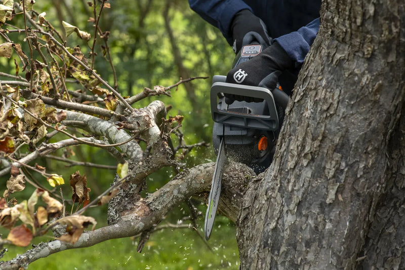 Introducing the Husqvarna Aspire™ Chainsaw 18V: a battery-powered tool ideal for DIY projects, featuring a sleek silver blade with "Husqvarna" branding, an ergonomic black body, and vibrant orange controls.