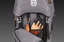 A versatile gray Husqvarna Gear backpack 70L with multiple pockets and orange accents, prominently displaying the Husqvarna logo on the front. A small green first aid symbol is near the bottom, making it ideal for climbing gear. The bag is set against a black background.