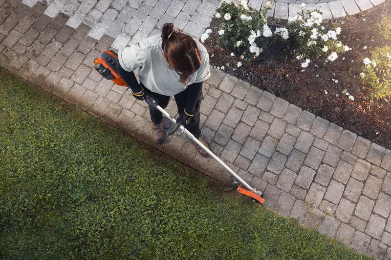 An orange and grey Husqvarna 525iLK Combi Trimmer (skin) with a long handle, a looped grip, and a protective cover on the cutting end. Ideal for maintaining gardens and lawns, this powerful trimmer features a battery pack at the back for cordless operation.
