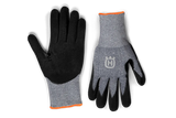 The Husqvarna Gloves - Technical Grip from Husqvarna are displayed against a black background. The gloves feature grey fabric on the top side adorned with a white emblem, while the palm side is made of black fabric. Orange trim accents are visible around the wrist cuffs. The left glove, ideal for gardening and providing excellent tactile sensitivity, is shown palm up, while the right glove is shown palm down.