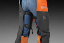 The Husqvarna Functional Safety Chaps, designed in bright orange and black for enhanced safety, feature durable fabric with reinforced areas. The high-visibility "Husqvarna" brand name is prominently displayed on the left thigh. These chaps offer an adjustable fit and boast a modern, rugged look ideal for outdoor work.