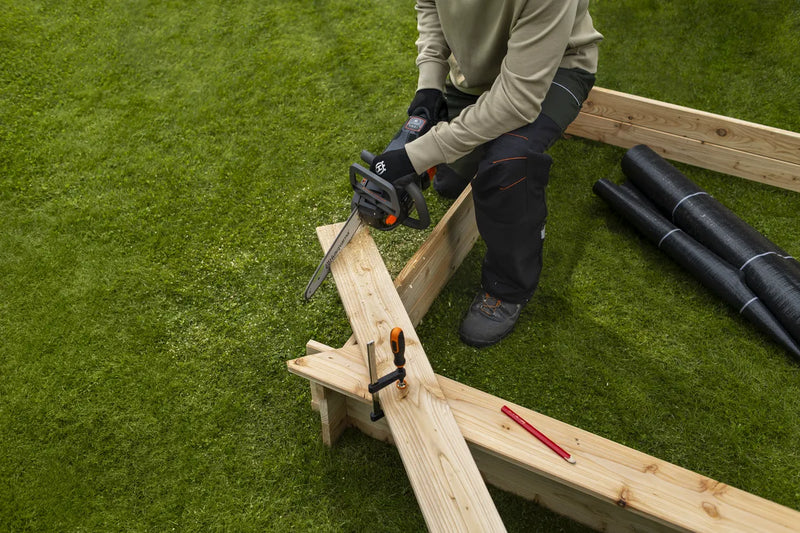 Introducing the Husqvarna Aspire™ Chainsaw 18V: a battery-powered tool ideal for DIY projects, featuring a sleek silver blade with "Husqvarna" branding, an ergonomic black body, and vibrant orange controls.