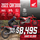 The Honda CRF300 Rally is a red and black adventure motorcycle with a windscreen, off-road tires, and blue & white accents. Designed for rugged terrain, it is highlighted on a plain white background, showcasing its sleek design and impressive off-road performance.