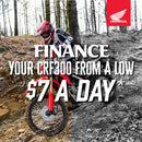 The Honda CRF300 Rally is a red and black adventure motorcycle with a windscreen, off-road tires, and blue & white accents. Designed for rugged terrain, it is highlighted on a plain white background, showcasing its sleek design and impressive off-road performance.
