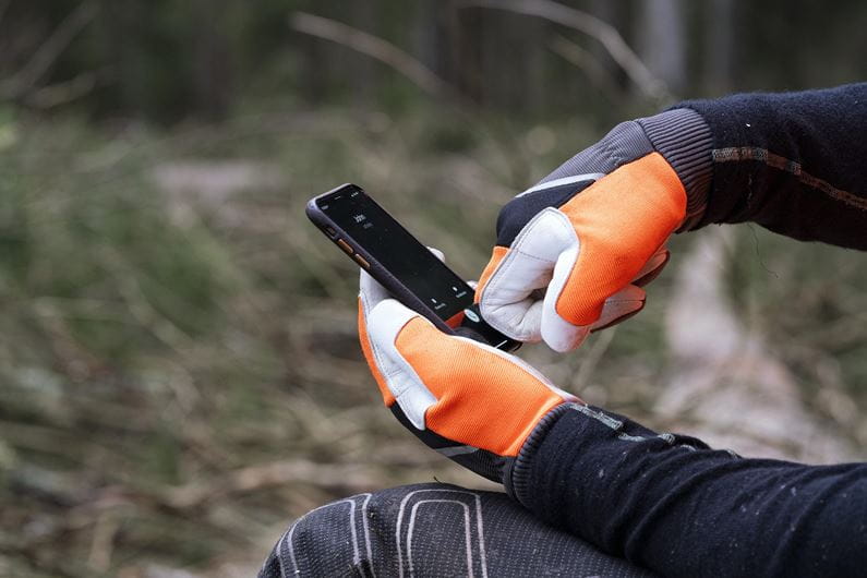 The Husqvarna Functional Gloves with saw protection, by Husqvarna, combine gray, white, black, and orange coloring. The left glove is displayed palm-up while the right glove is displayed palm-down. Both gloves feature a prominent gray logo on the wrist area and have ribbed cuffs for a secure fit.