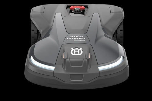 The Husqvarna Automower 430X NERA is a sleek, grey robotic lawn mower featuring two large wheels at the rear and two smaller wheels at the front. It boasts a red stop button on top, LED headlights, and proudly displays the Husqvarna logo on the front. With its modern design, this mower is equipped with object avoidance technology and can be conveniently controlled via the Automower Connect app.