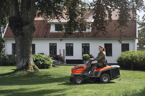 The Husqvarna Battery TC 100i Tractor in bright orange and black features a steering wheel, comfortable seat, efficient collecting system, and durable tires. It boasts sleek lines and a modern design for dynamic mowing.