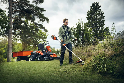 A Husqvarna 325iR Brushcutter (skin) lays on a white background. Perfect for lawns and other outdoor maintenance, the tool features a long silver shaft with a black handle at the top and an orange cutting head at the bottom. The motor is housed in an orange casing near the handle.