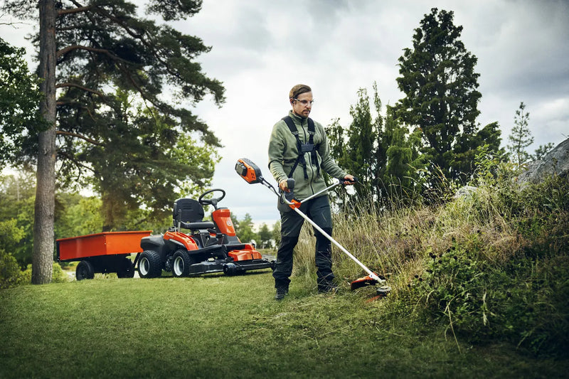 A Husqvarna 325iR Brushcutter (skin) lays on a white background. Perfect for lawns and other outdoor maintenance, the tool features a long silver shaft with a black handle at the top and an orange cutting head at the bottom. The motor is housed in an orange casing near the handle.