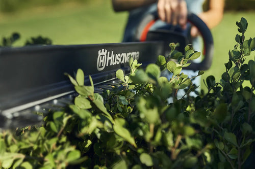 This image features a Husqvarna Aspire™ H50 Hedge Trimmer (Kit) with an 18V battery, perfect for outdoor tasks. The trimmer has an ergonomic black handle with orange accents, a long cutting blade, and is part of the "Power for All" Alliance.