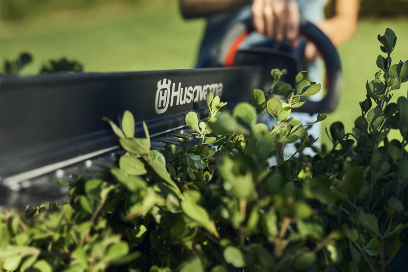 This image features a Husqvarna Aspire™ H50 Hedge Trimmer (Kit) with an 18V battery, perfect for outdoor tasks. The trimmer has an ergonomic black handle with orange accents, a long cutting blade, and is part of the "Power for All" Alliance.