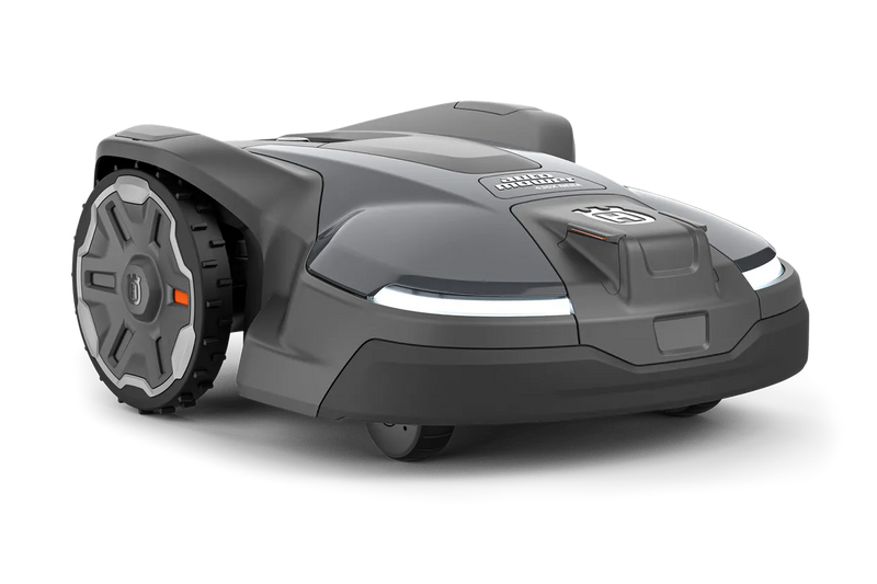The Husqvarna Automower 430X NERA is a sleek, grey robotic lawn mower featuring two large wheels at the rear and two smaller wheels at the front. It boasts a red stop button on top, LED headlights, and proudly displays the Husqvarna logo on the front. With its modern design, this mower is equipped with object avoidance technology and can be conveniently controlled via the Automower Connect app.