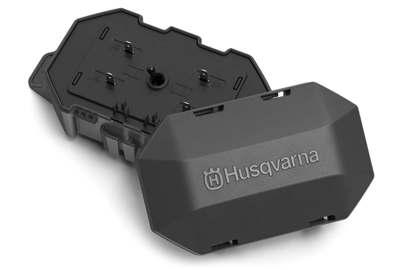 The Husqvarna Automower® Area Switch, enclosed in a gray plastic rectangular casing with a detachable cover, features the Husqvarna logo on top and includes various mounting points and connectors for electronic components. This shell is integral to the Husqvarna Automower, specifically designed to manage the boundary wire and Area Switch configurations.