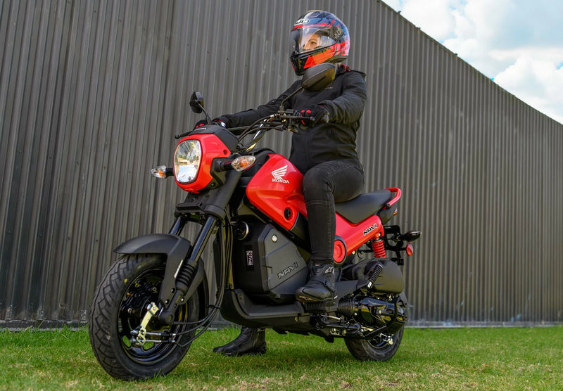 The Honda NAVi NVA110, by Honda, is a vibrant red mini motorcycle that emphasizes urban mobility with its compact design. It features a sleek black seat and the iconic Honda logo prominently displayed on its fuel tank. Equipped with thick black wheels and a short exhaust, this model expertly combines elements of a scooter and motorcycle to create an efficient ride ideal for city streets.