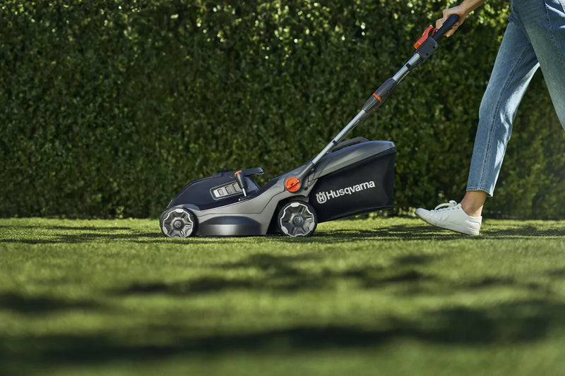 A black and gray Husqvarna Aspire™ L34 Lawn Mower (Skin) with an 18V system is shown. Featuring a sleek, lightweight, and foldable design with adjustable handle heights and orange accent details, it fits effortlessly into your storage space. A graphic in the lower right corner displays "Power for ALL 18V," indicating its battery compatibility.