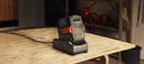 The Husqvarna 40-C80 Battery Charger, in gray, features an attached cable and a slot for the battery, prominently displaying the Husqvarna logo on the front. Designed for efficient charging, this compact single bay charger boasts an angled design, making it ideal for portable use.