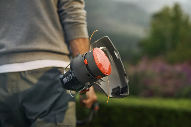 The Husqvarna Aspire™ T28 Grass Trimmer (Kit) features a long, extendable handle and a cutting blade at the end, with ergonomic grips and an orange and black design. A red "POWER FOR ALL" 18V Alliance logo is displayed in the lower left corner, highlighting its versatility as a battery trimmer.