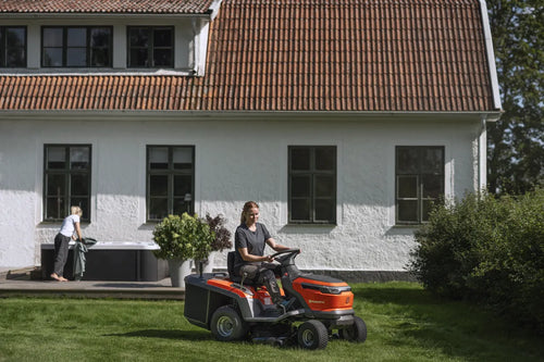 The Husqvarna Battery TC 100i Tractor in bright orange and black features a steering wheel, comfortable seat, efficient collecting system, and durable tires. It boasts sleek lines and a modern design for dynamic mowing.