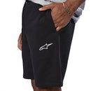A person wearing Alpinestars Rendition Fleece Shorts in black features a white logo on the left thigh, standing casually with one hand in the pocket. The shorts by Crown Kiwi Enterprises Limited have an elastic waistband and perfectly complement a light gray shirt. The plain white background accentuates the sporty Alpinestars vibe.