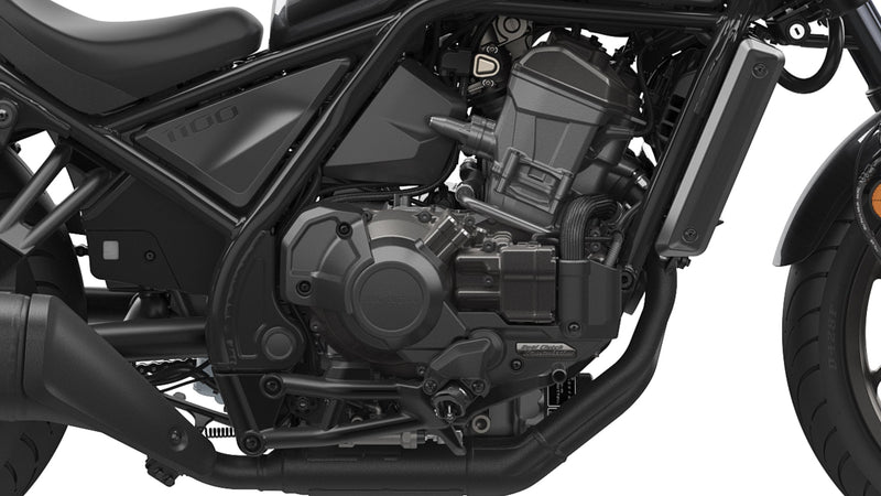 A black Honda Rebel CMX1100 DCT motorcycle is shown in profile against a white background. The cruiser class bike features a low seat, wide handlebars, and a robust engine with automatic transmission. It boasts a modern, minimalist design with sleek lines and a matte finish, including spoked wheels and disc brakes.