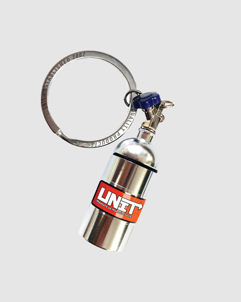 A UNIT Oxide Keyring featuring a miniature blue nitrous oxide bottle with a silver ring and a screw top storage compartment. The bottle has a valve at the top and a branded logo sticker on the side that reads "NITROUS" in bold white letters on a red and white background.