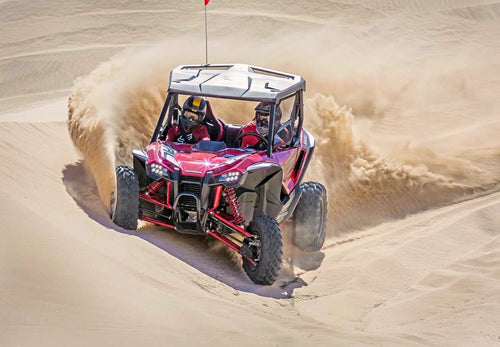 A red Honda Talon R off-road vehicle is pictured. It features robust, large tires, a roll cage, and sporty accents. The vehicle has a rugged design suitable for rough terrain, with visible shock absorbers and a roof for protection—perfect for sport side-by-side enthusiasts.