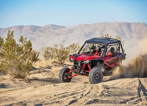 A red Honda Talon R off-road vehicle is pictured. It features robust, large tires, a roll cage, and sporty accents. The vehicle has a rugged design suitable for rough terrain, with visible shock absorbers and a roof for protection—perfect for sport side-by-side enthusiasts.