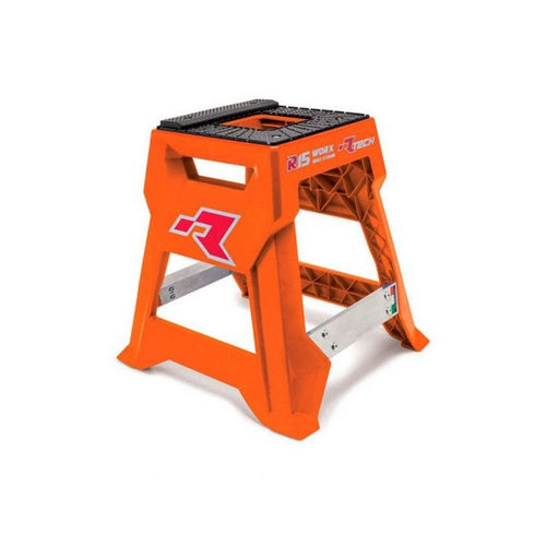 An orange plastic step stool, the RTECH R15 Works Cross Bike Stand Launch Edition, features metal reinforcements and a black, textured top for grip. It showcases the branded design with the letter "R" and the words "RS Work" and "RS2N." With its non-slip pyramid frame and triangular support patterns for stability, it ensures maximum load capacity.