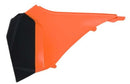 The AIR BOX COVER RTECH LEFT HAND for KTM models boast an orange and black plastic geometric design akin to KTM's style, featuring sharp edges and visible mounting tabs on the inner side.