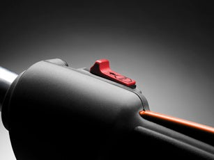 A gas-powered orange and white Husqvarna 129LK Combi Trimmer with a long white pole and a black handle. Perfect for the outdoors, the powerful engine is on one end while the cutting head, equipped with an orange protective cover, is on the other.