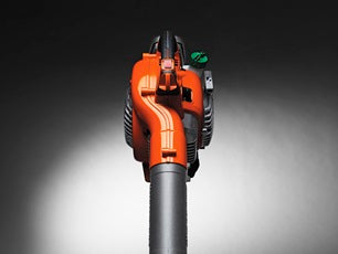 A Husqvarna 125B Blower with an orange and black design, perfect for garden tasks. The machine features a long nozzle for directing airflow and a small white fuel tank attached to the back. The engine compartment is visible with air vents on the side, making it ideal for any outdoor setting.