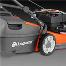 An orange and black Husqvarna LC419A Lawn Mower with a grass collection bag on the rear. Perfect for any outdoors enthusiast, this power tool features a push handle, four wheels, and a metal cutting deck. The Husqvarna logo is prominently displayed on the side of the bag.