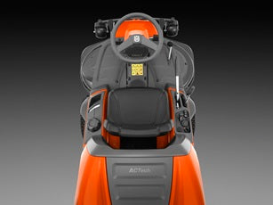 A modern, orange and black Husqvarna RC320TS AWD Rider Mower - Grass collecting with a high-backed seat, steering wheel, and dual headlights. Designed for power and performance, the mower features sturdy wheels and a cutting deck beneath the front. The brand logo is visible on the front and side of the mower.