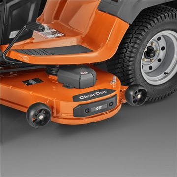 A Husqvarna TS242TXD Ride-On Mower is shown in bright orange, featuring a comfortable gray seat with armrests, large textured tires, and a robust ClearCut™ deck underneath. The side discharge tractor boasts a modern design with the prominent Husqvarna logo on its front.