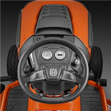 A Husqvarna TS242TXD Ride-On Mower is shown in bright orange, featuring a comfortable gray seat with armrests, large textured tires, and a robust ClearCut™ deck underneath. The side discharge tractor boasts a modern design with the prominent Husqvarna logo on its front.