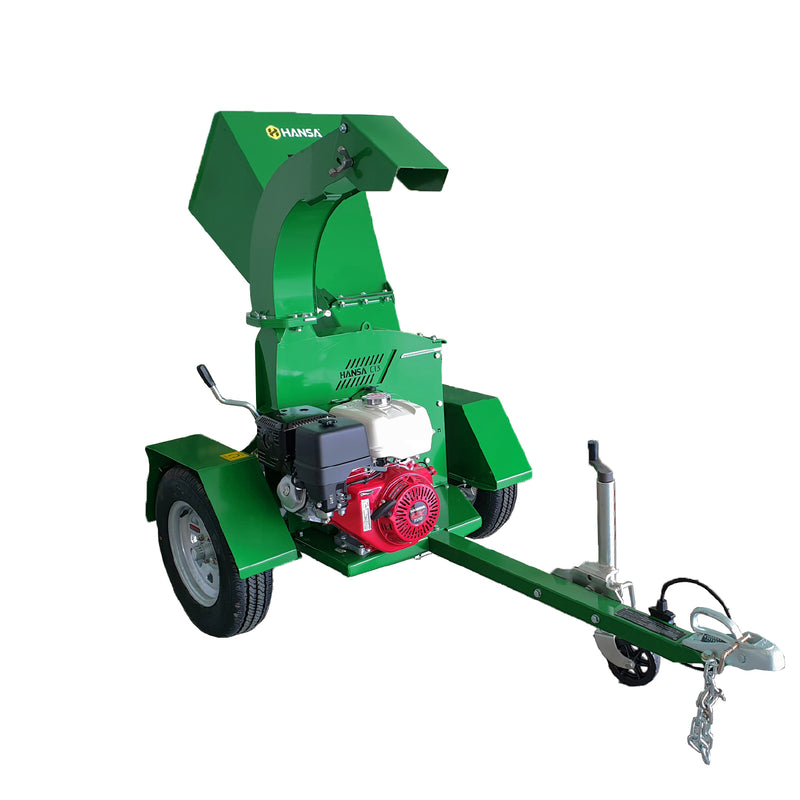 The green, towable Hansa C13 Road Tow Swivel Outlet features a large funnel-shaped hopper for feeding branches and a discharge chute for ejecting wood chips, making it ideal for maintaining lawns and gardens. It has a red engine mounted on the front, large wheels, and a tow hitch for easy vehicle attachment.