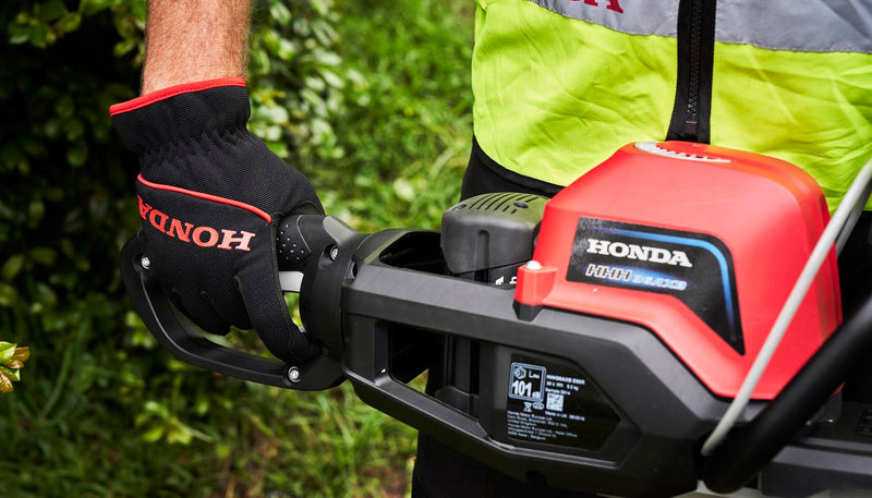 A red and black cordless Honda HHH36 Battery Hedge Trimmer Kit from Honda Power Equipment with a long dual-action blade and ergonomic handle, perfect for gardens. The tool features a safety guard and controls on the top housing.