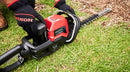 A red and black cordless Honda HHH36 Battery Hedge Trimmer Kit from Honda Power Equipment with a long dual-action blade and ergonomic handle, perfect for gardens. The tool features a safety guard and controls on the top housing.