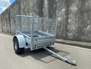 A City Honda Manawatu Custom Built Caged ATV Trailer is parked on a concrete surface. The trailer's tongue is extended and rests on the ground, beside several Honda generators. A weathered concrete wall forms the backdrop.