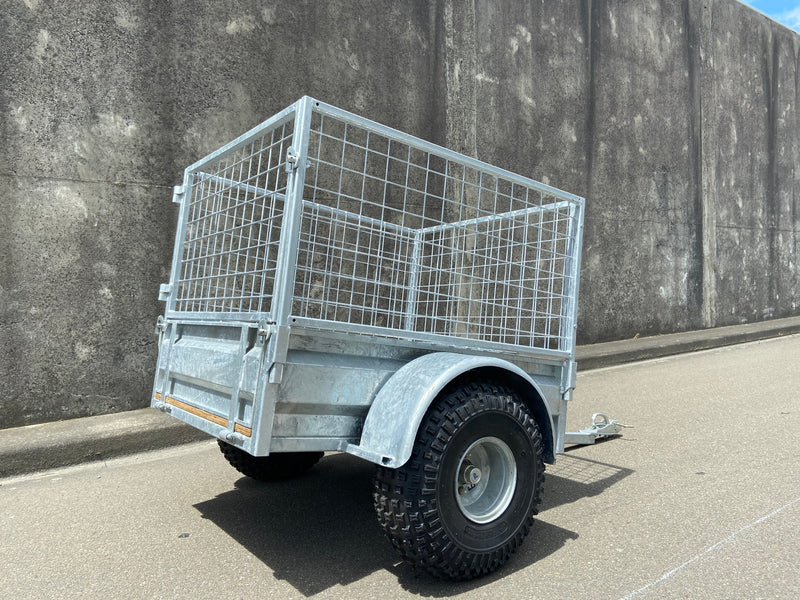 A City Honda Manawatu Custom Built Caged ATV Trailer is parked on a concrete surface. The trailer's tongue is extended and rests on the ground, beside several Honda generators. A weathered concrete wall forms the backdrop.