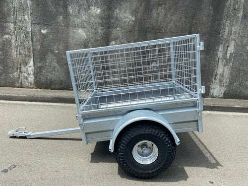 A City Honda Manawatu Custom Built Caged ATV Trailer is parked on a concrete surface. The trailer's tongue is extended and rests on the ground, beside several Honda generators. A weathered concrete wall forms the backdrop.