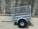 A City Honda Manawatu Custom Built Caged ATV Trailer is parked on a concrete surface. The trailer's tongue is extended and rests on the ground, beside several Honda generators. A weathered concrete wall forms the backdrop.
