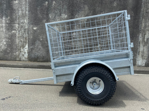 A City Honda Manawatu Custom Built Caged ATV Trailer is parked on a concrete surface. The trailer's tongue is extended and rests on the ground, beside several Honda generators. A weathered concrete wall forms the backdrop.