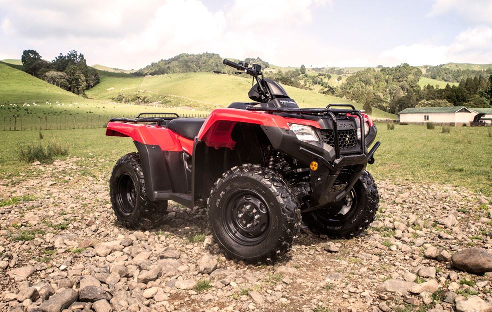 The Honda TRX420FM2, an all-terrain vehicle (ATV) in a striking red color, boasts large, knobby tires and a sturdy suspension system. This ATV also features a black seat, handlebar with controls, cargo racks on both the front and rear ends, rugged fenders, and advanced Electronic Power Steering (EPS). Designed by Honda for off-road use, this vehicle is built to tackle challenging terrains with ease.
