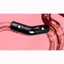 A close-up image showcases the Akrapovic Heat Shield CA, crafted from black carbon fiber and mounted on shiny, curved copper or bronze exhaust pipes against a pink background. The heat shield features two visible bolt fastenings and a small AKRAPOVIC logo. This AKRAPOVIC system fits various models.
