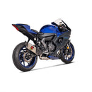 The Akrapovic Full System YZF R7 2021-23 is a sleek silver titanium racing exhaust for motorcycles, featuring dual pipes and a carbon fiber cover. It has the iconic AKRAPOVIC logo in red and yellow, includes mounting brackets, and highlights Akrapovič dyno performance.